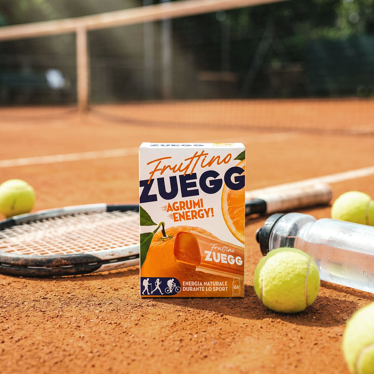 Packaging Fruttino Zuegg Agrumi Energy — snack sportivo a base di frutta in lifestyle shot campo da tennis | Design Collective